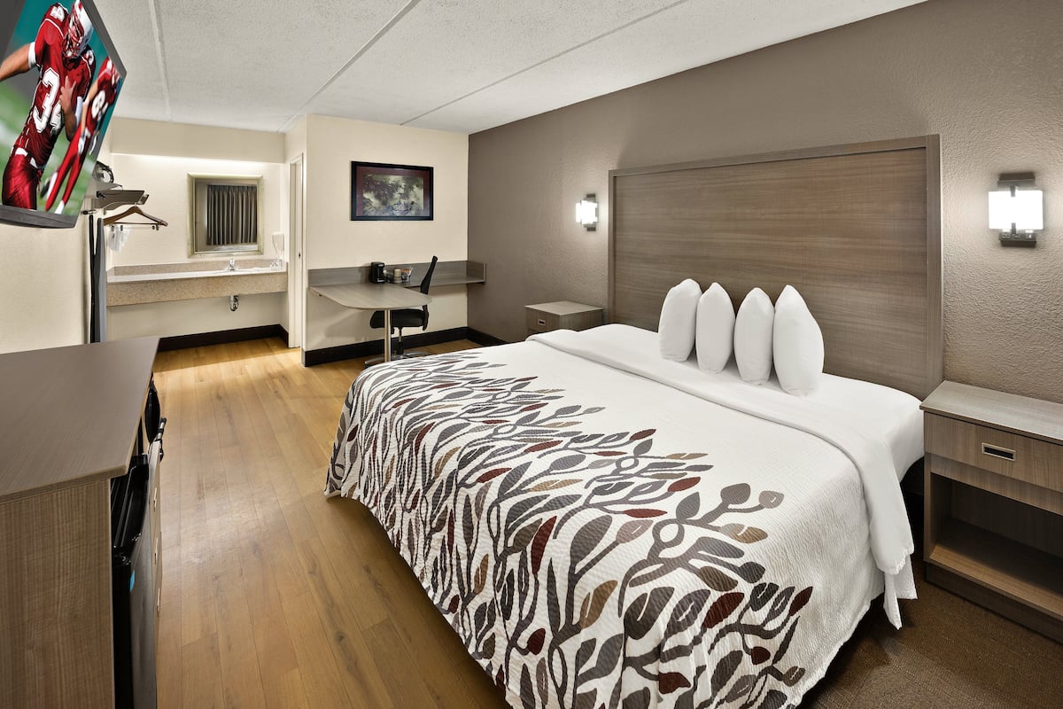 A hotel room with a bed, bedside tables, a desk, a chair, and a mirror.