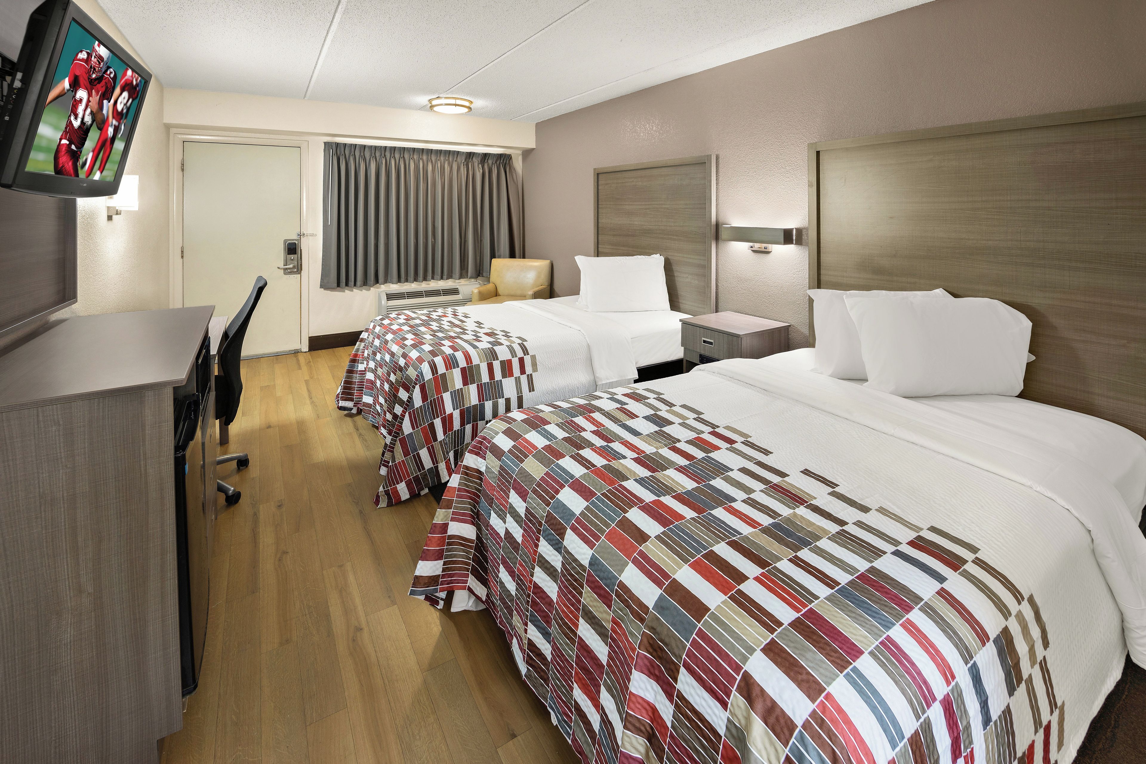 Habitación de hotel con dos camas, un escritorio, una silla, un televisor y una ventana con cortinas.