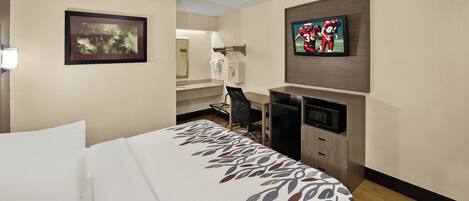 A hotel room with a bed, a desk, a television, and a minibar.