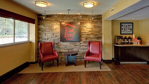 A Red Roof Inn lobby with two leather chairs, a stone wall, a coffee station, and a framed photo collage on the wall. - Red Roof Inn Chapel Hill - UNC (Durham)