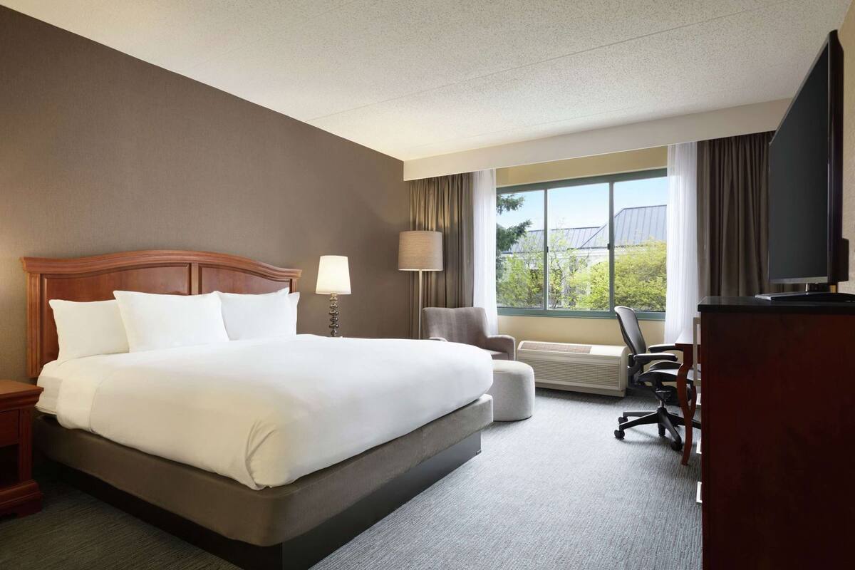 Ein Hotelzimmer mit einem großen Bett, einem Schreibtisch, einem Stuhl, einer Lampe und einem Fernseher.