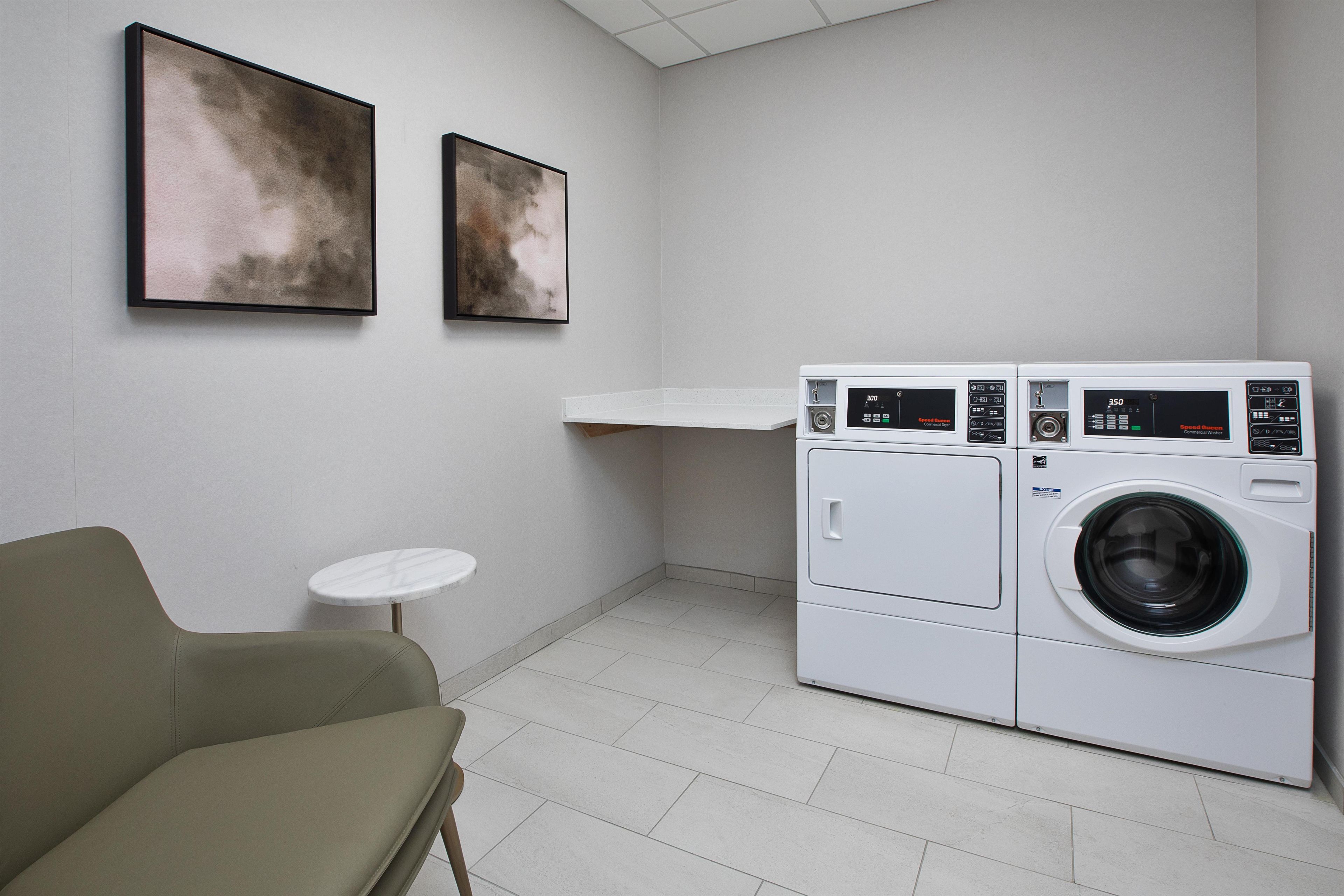 Een wasserette met een wasmachine, een klein tafeltje en twee ingelijste kunstwerken aan de muur.