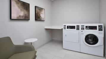 Een wasserette met een wasmachine, een klein tafeltje en twee ingelijste kunstwerken aan de muur.
