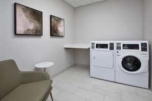 A laundry room with a washing machine, a small table, and two framed artworks on the wall.