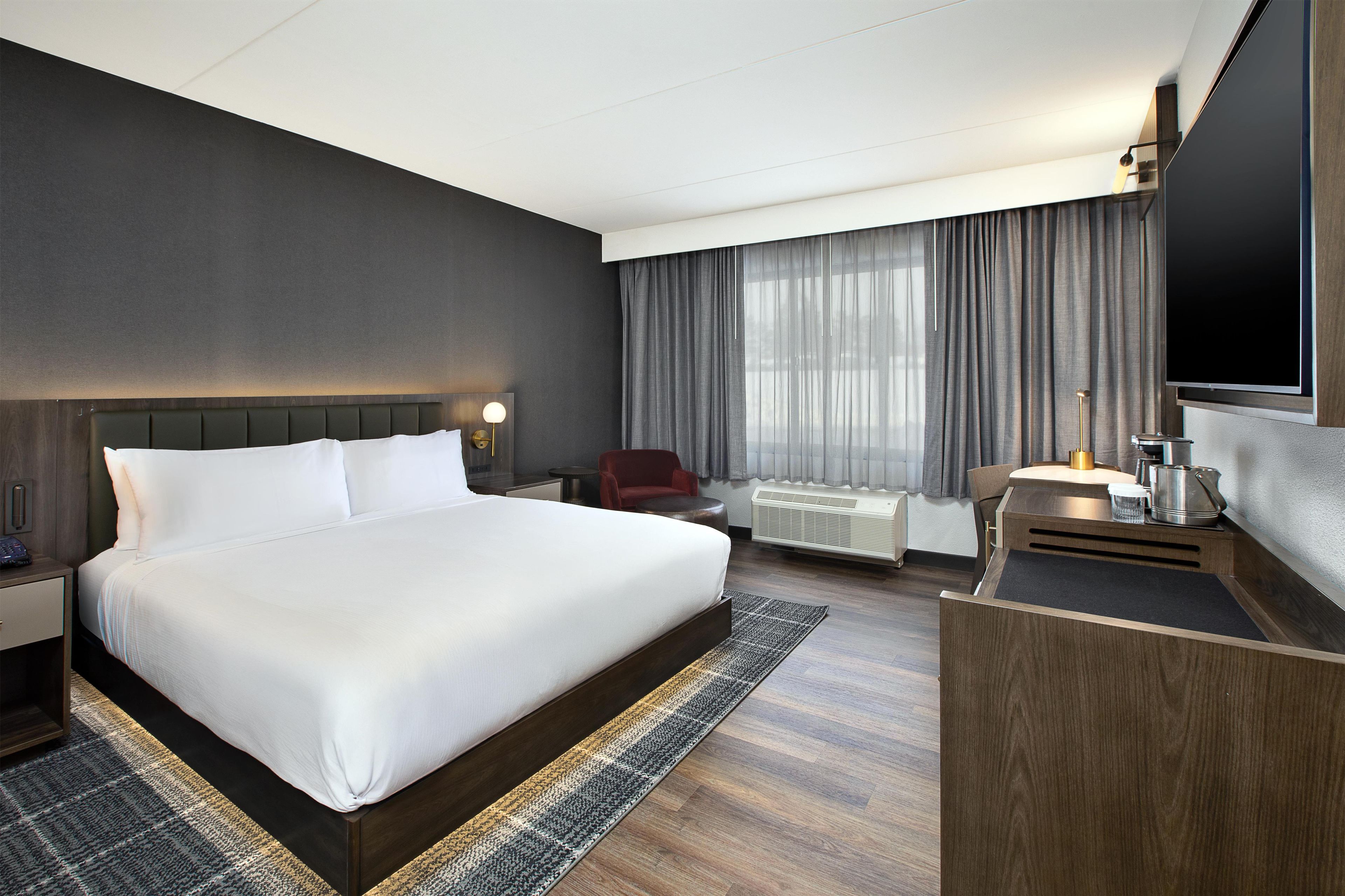 A hotel room with a large bed, a desk, a chair, a TV, and a window with curtains.