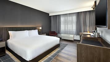 A hotel room with a large bed, a desk, a chair, a TV, and a window with curtains.
