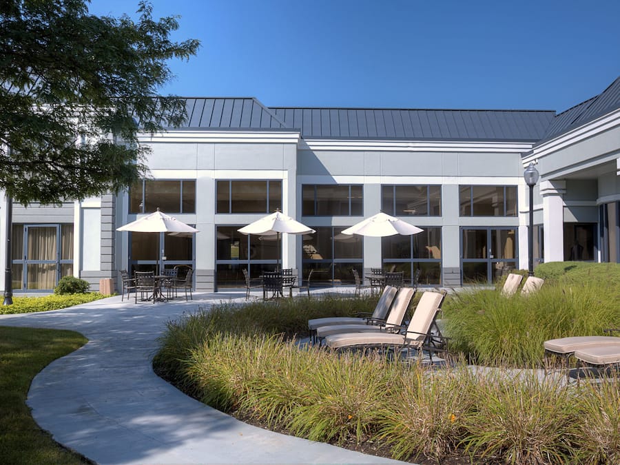 A building with a covered outdoor seating area, large windows, and a pathway leading to the entrance.