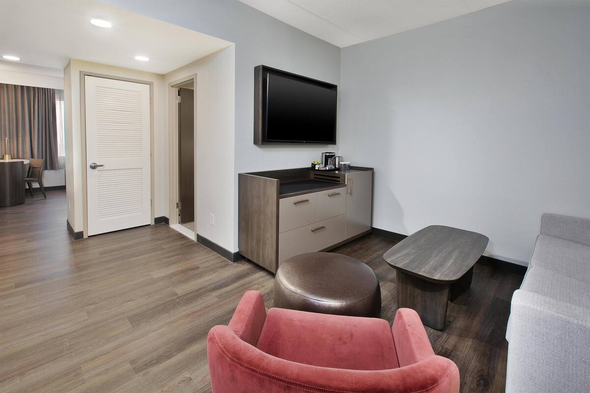 Ein modernes Wohnzimmer mit Flachbildfernseher, Holzschrank, rotem Sessel, grauem Sofa und einer Holzbank.