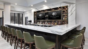 Un espace bar doté d’un comptoir en marbre, de tabourets de bar verts et d’une enseigne DoubleTree by Hilton.
