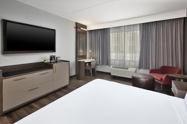 A hotel room with a large bed, a desk with a chair, a flat-screen TV, a coffee maker, and a window with curtains.