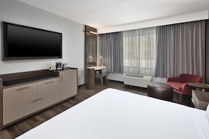 Habitación de hotel con una cama grande, un escritorio con silla, televisor de pantalla plana, cafetera y ventana con cortinas.