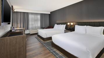 A hotel room with two beds, a TV, a desk, and a large window with curtains.