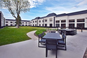 A courtyard with outdoor seating, a lawn, and a building with large windows and a flat roof.