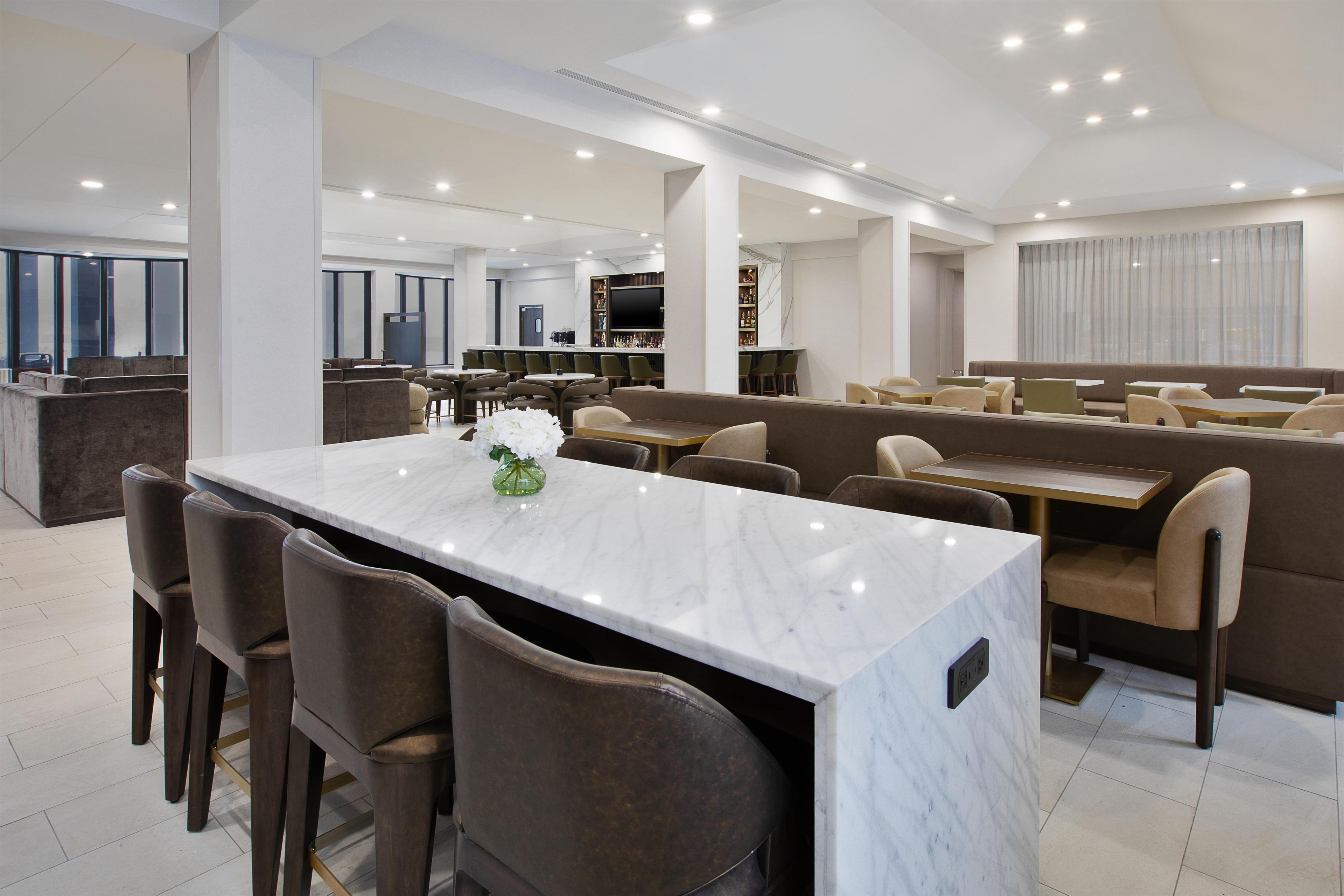 A modern hotel lobby with a marble reception desk, seating areas, and a bar.