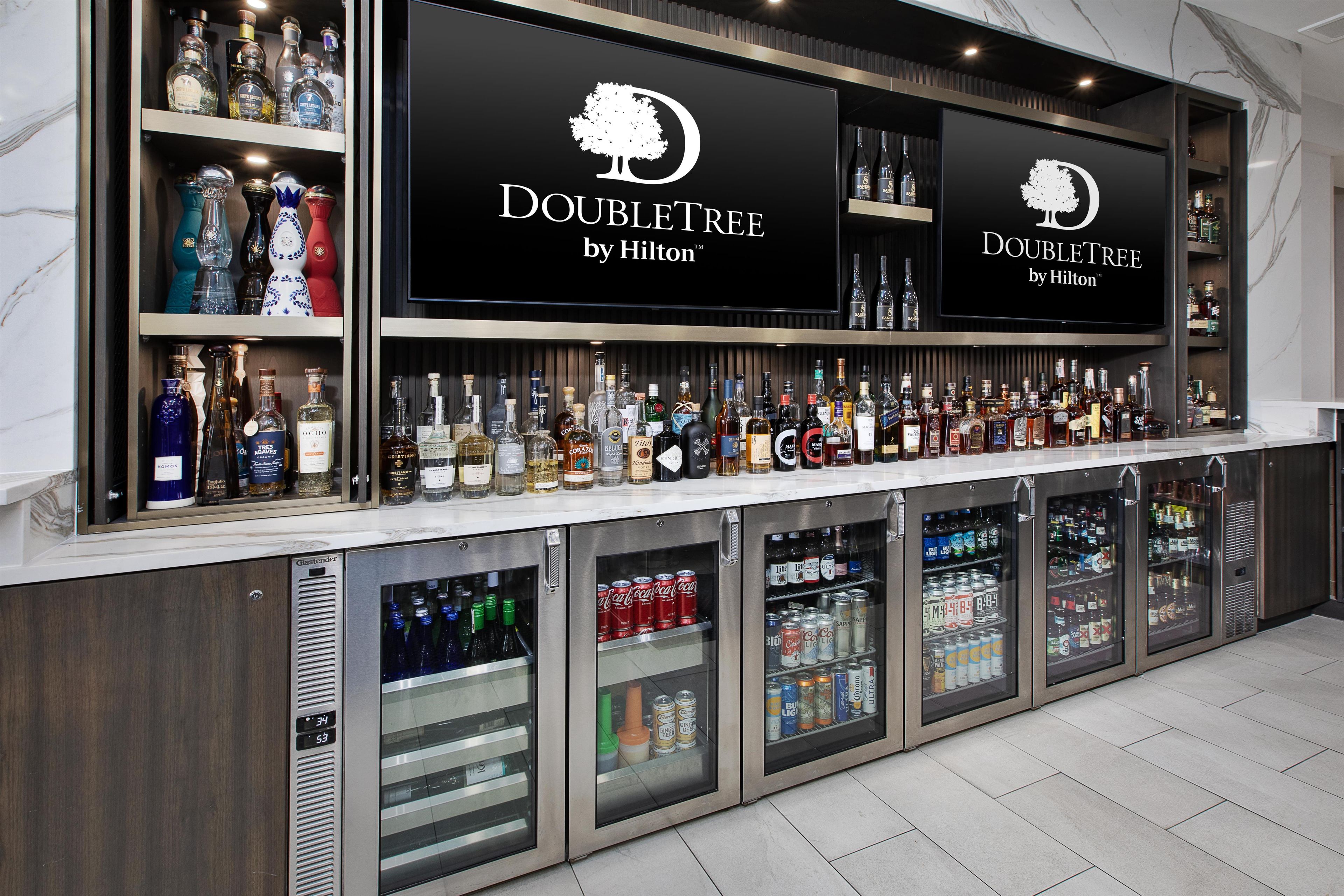 A bar area with a variety of liquor bottles and canned beverages, featuring the DoubleTree by Hilton logo.