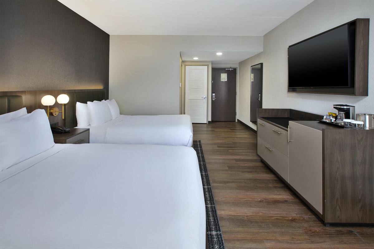 Ein Hotelzimmer mit zwei Betten, einem Flachbildfernseher, einer Minibar und Holzboden.