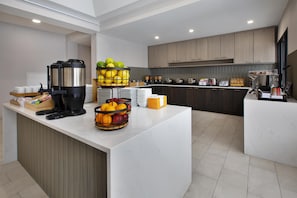 A modern kitchen with a central island, equipped with a coffee machine, fruit bowls, and a buffet setup. - DoubleTree by Hilton Detroit Novi (Novi)