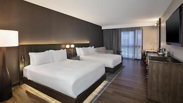 A hotel room with two beds, a desk, a TV, and a large window with curtains.