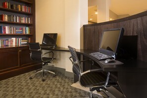 A modern office cubicle with a desk, two chairs, a computer, and a bookshelf filled with books. - DoubleTree by Hilton Detroit Novi (Novi)