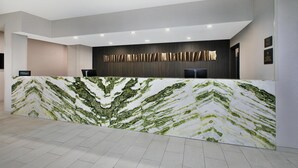 Un comptoir d’accueil moderne au design évoquant le marbre, doté d’un téléviseur à écran plat et agrémenté d’un mur foncé orné de lignes verticales.