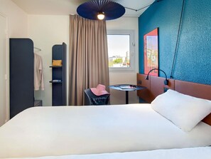 A hotel room with a bed, a small table, a chair, a window, and a curtain. - ibis Marseille Timone (Marseille)