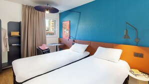 A hotel room with a bed, a desk, a chair, a small table, a window with curtains, and a wall with a painting. - ibis Marseille Timone (Marseille)