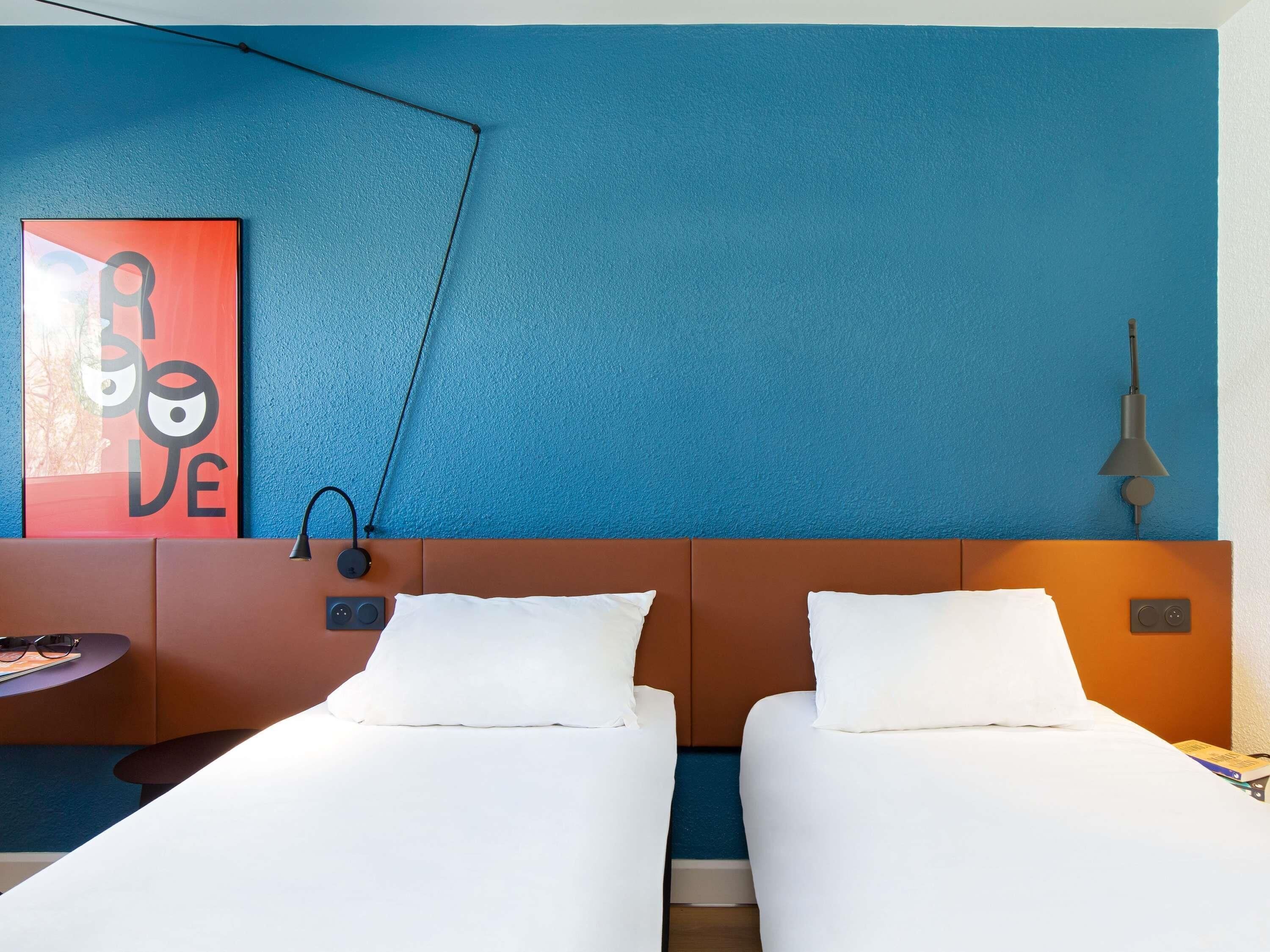 Ein Hotelzimmer mit zwei Einzelbetten, einer Wandlampe, einem Gemälde und einer Steckdose.