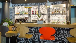 A bar area with a counter, bar stools, hanging pendant lights, and a wall with a black and white mural. - ibis Marseille Timone (Marseille)