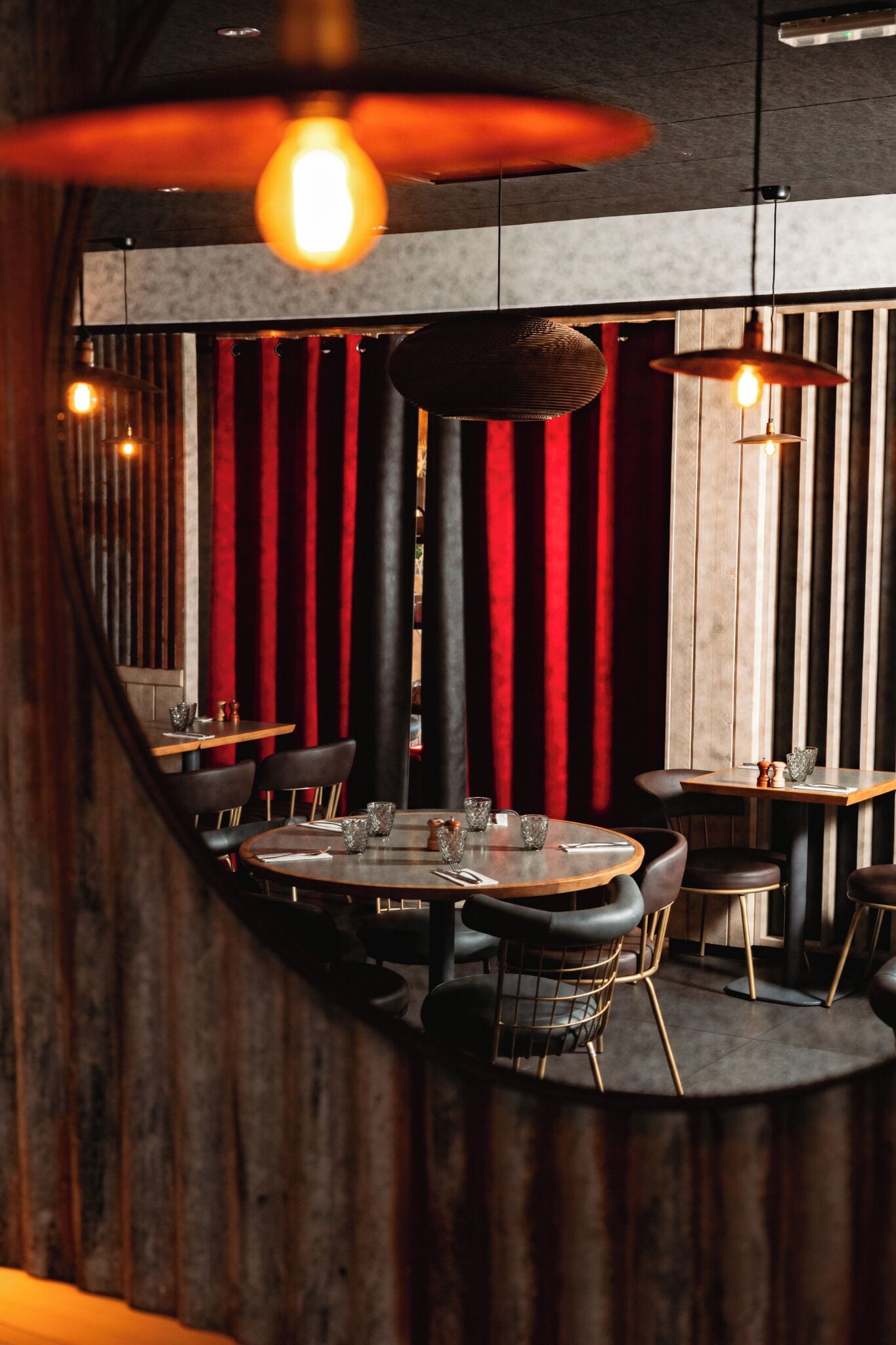 A restaurant interior with round tables, black leather chairs, and red curtains.