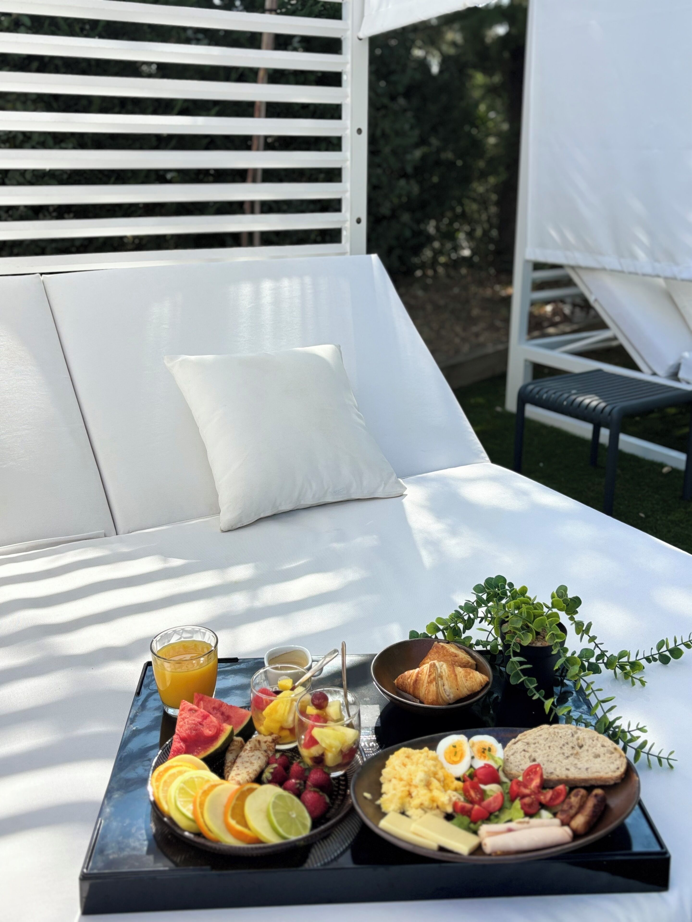 A breakfast tray with fruits, eggs, and bread on a table in a sunny outdoor setting.