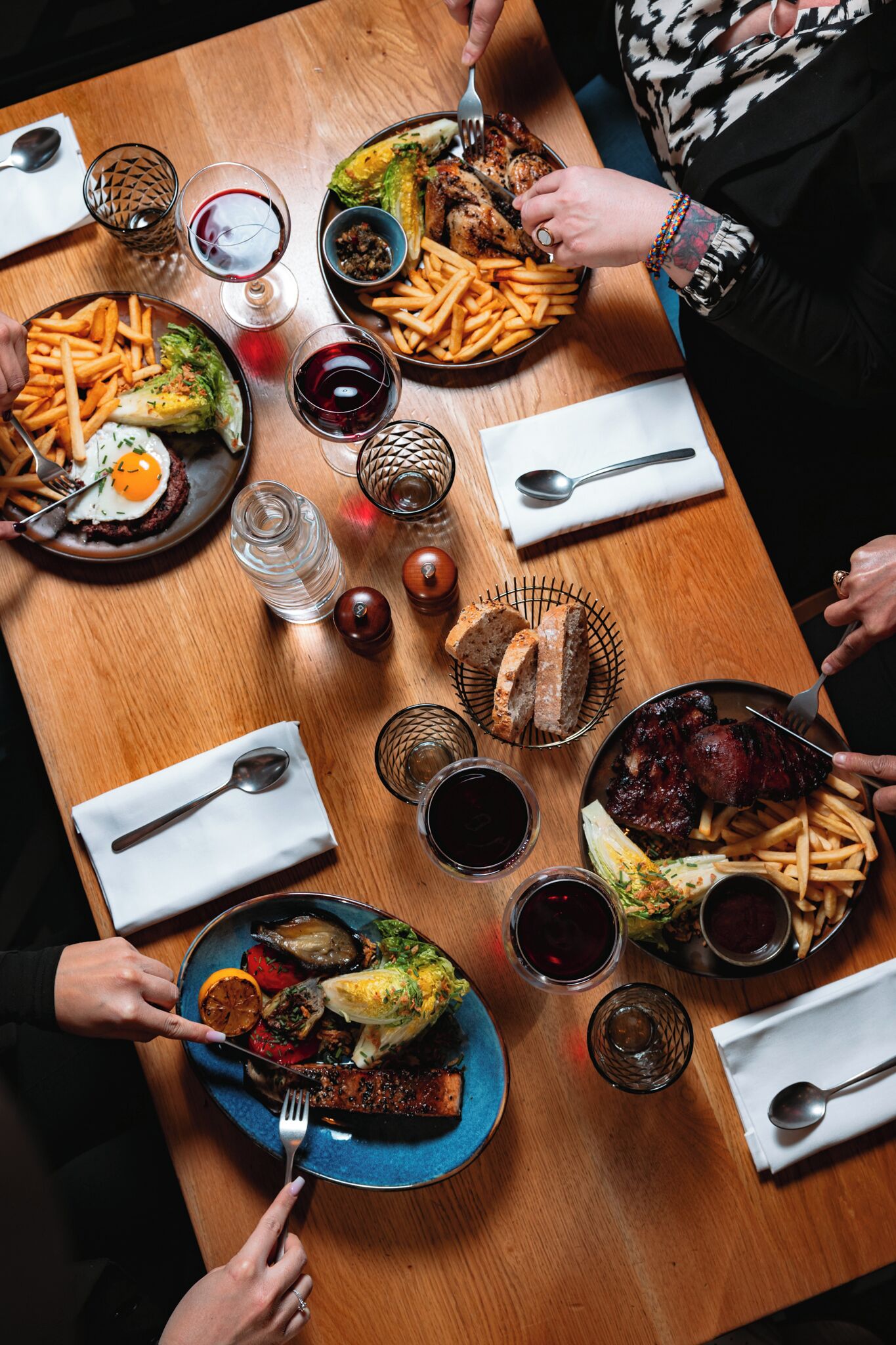 A wooden dining table with various dishes, including steak, fries, and a salad.