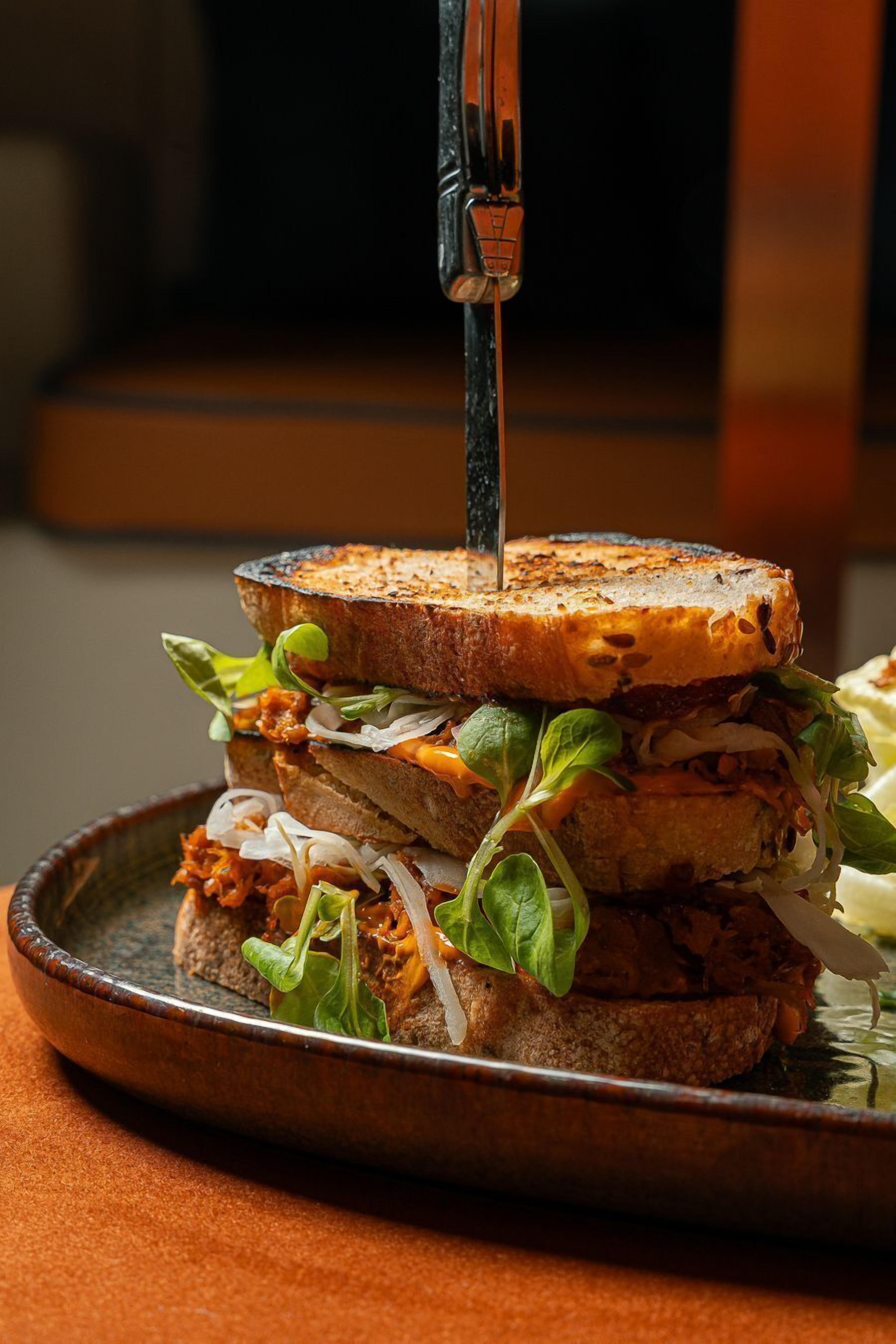 A grilled sandwich with a knife inserted into it, placed on a plate.