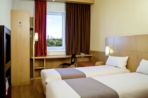 A hotel room with two beds, a desk with a chair, a telephone, and a window with curtains.
