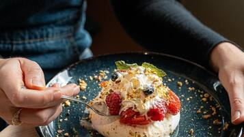 A person holding a plate with a dessert topped with berries and nuts, and a cup of coffee on the table.