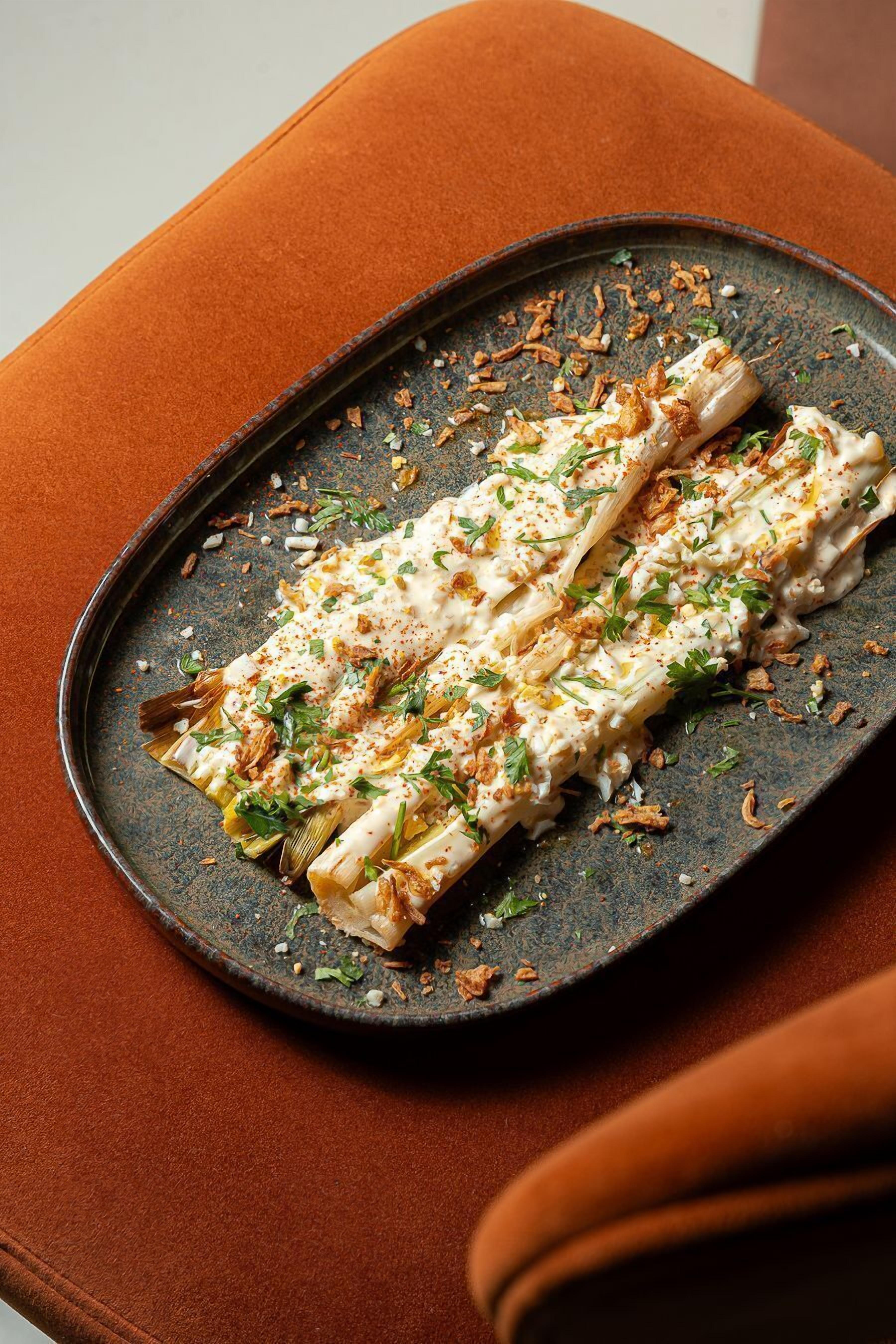 A plate of food on a dark ceramic plate with a rustic design, placed on a brown cushioned surface.
