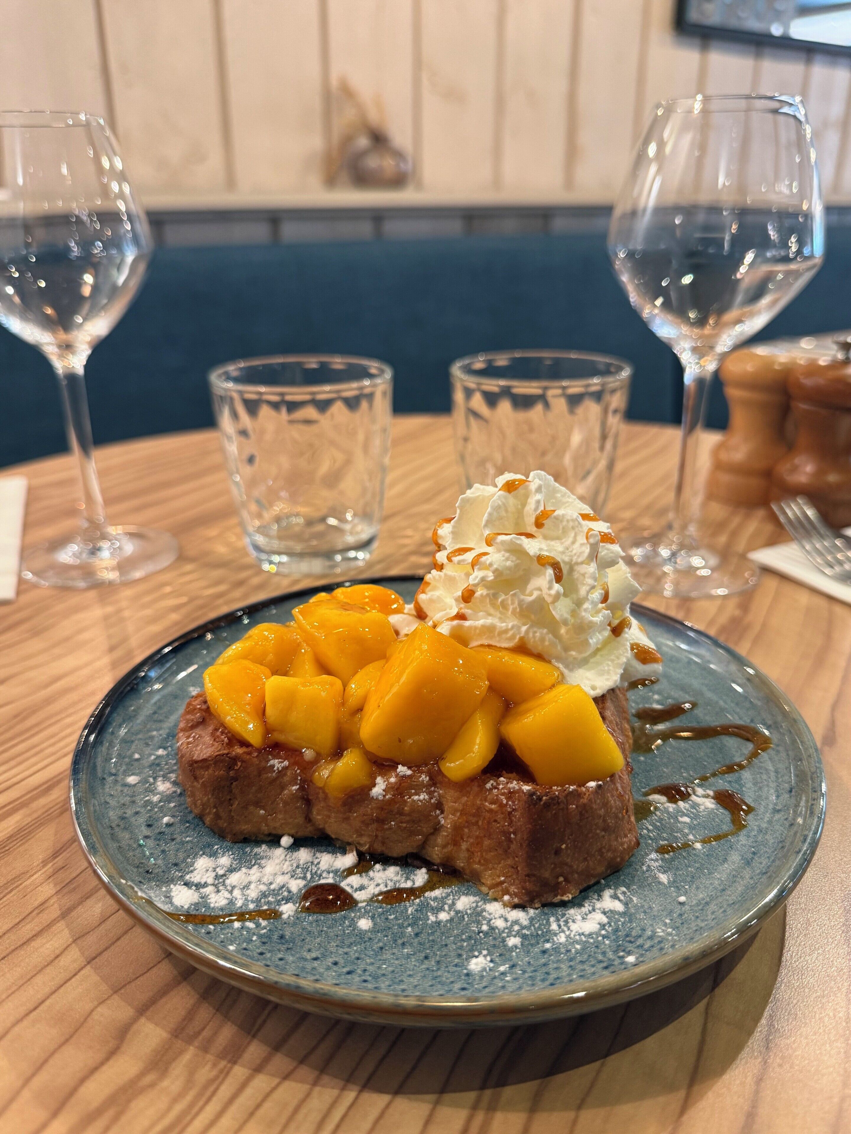 Un plato de postre con un pastel cubierto de fruta, crema batida y almíbar sobre un plato de cerámica azul.
