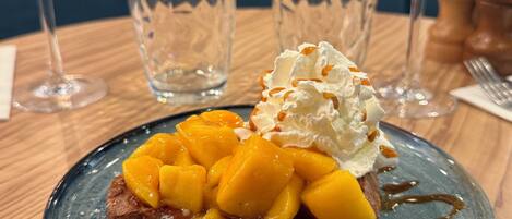 Un plato de postre con un pastel cubierto de fruta, crema batida y almíbar sobre un plato de cerámica azul.