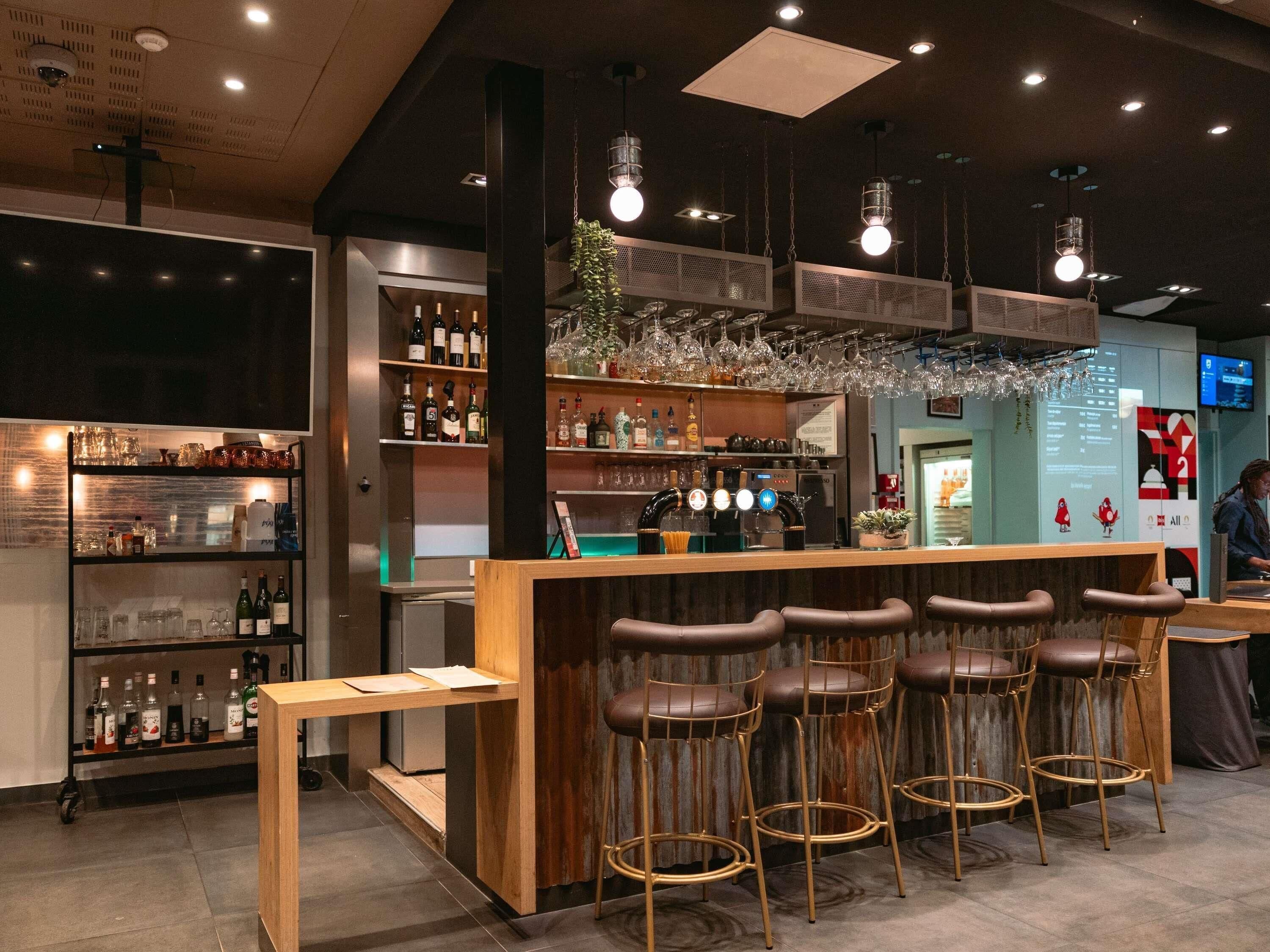 Een bar met krukken, flessenrekken en hangende lampen.