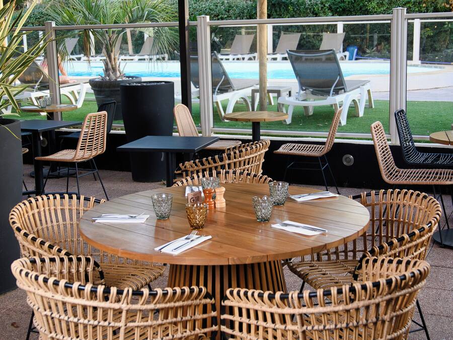 Eine Terrasse im Freien mit Korbmöbeln, einem runden Tisch und Blick auf einen Swimmingpool.
