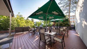 An outdoor patio with wooden flooring, tables, chairs, and green umbrellas. - Best Western Plus Hotel Steinsgarten (Giessen)