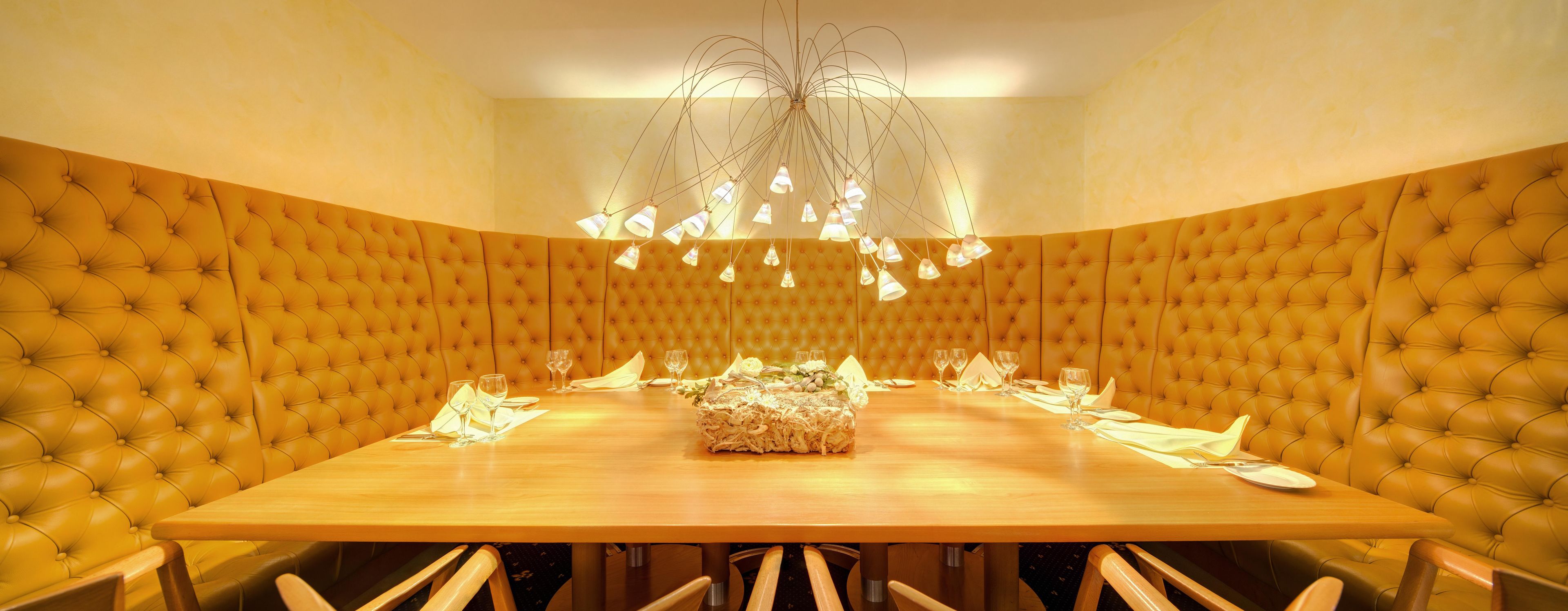 A dining area with a large wooden table, upholstered high-backed chairs, and a chandelier.