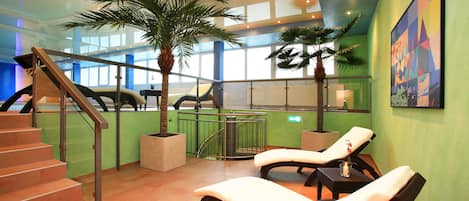 Un espacio interior moderno con una escalera, sillones de descanso y palmeras en macetas.