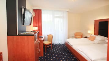 A hotel room with a bed, a desk with a chair, a TV mounted on the wall, and a window with curtains.