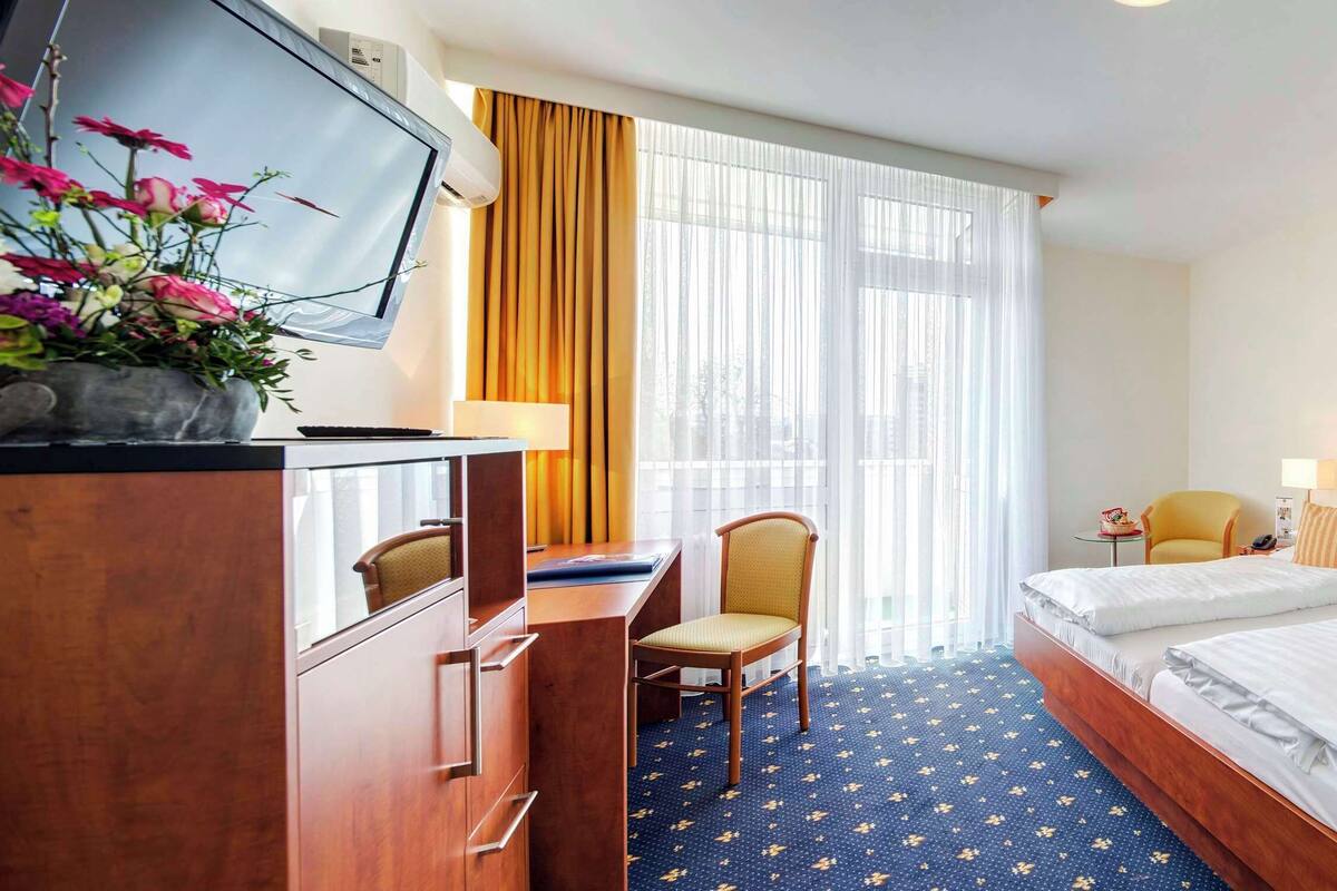 A hotel room with two beds, a desk with a chair, a TV, and a desk lamp.