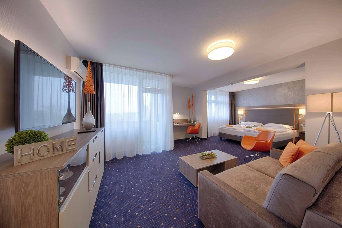 A hotel room with a bed, a desk, a chair, a sofa, and a TV.