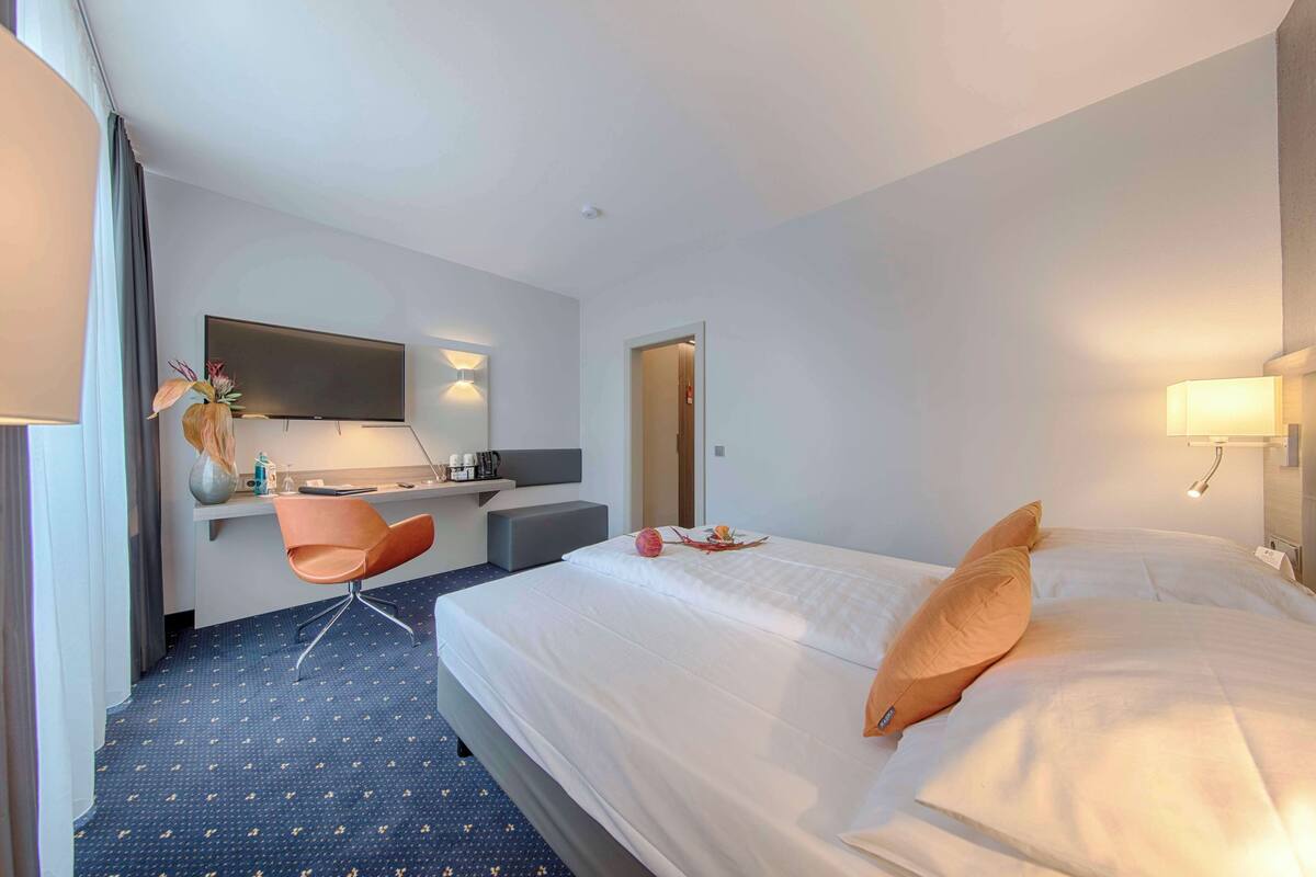 A hotel room with a bed, a desk, a chair, and a television.