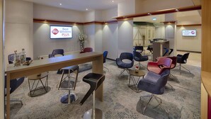 A hotel lobby with a reception desk, several chairs, a small table with a vase, and a sign on the wall. - Best Western Plus Hotel Steinsgarten (Giessen)