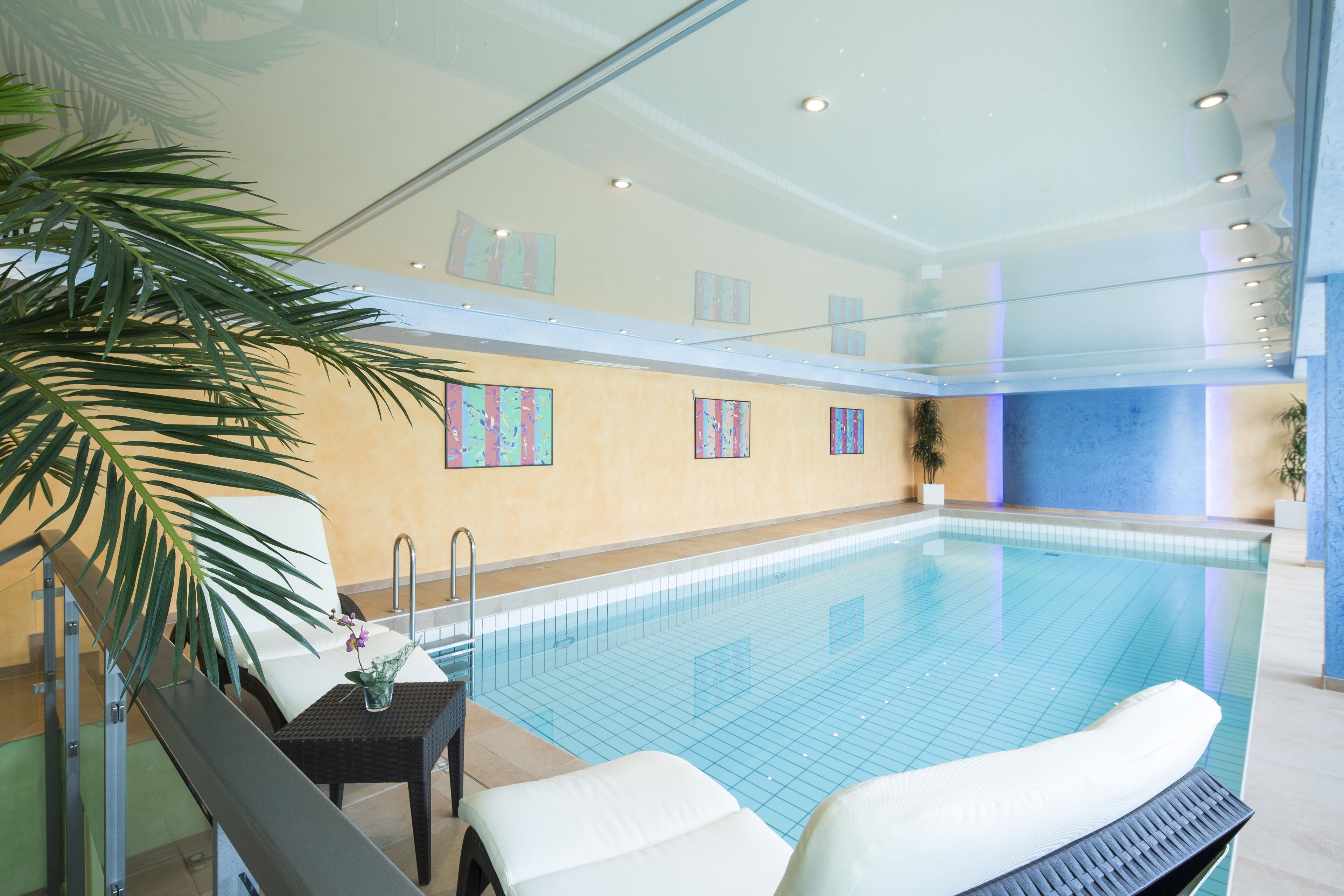 Une piscine intérieure avec un sol carrelé, un espace de détente aménagé au bord du bassin et un mur décoré d’œuvres d’art abstrait.