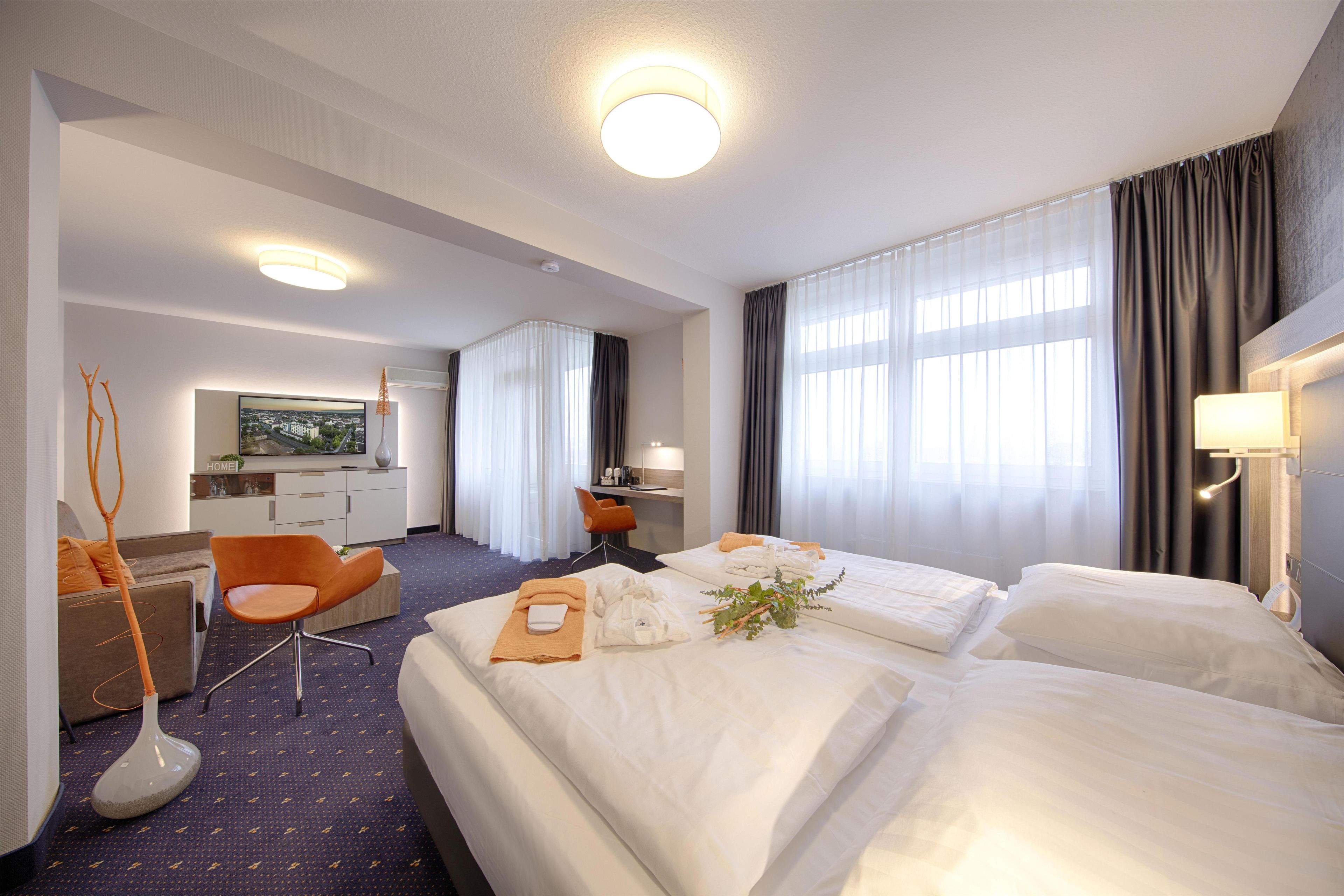 A hotel room with two beds, a desk, a chair, and a television.