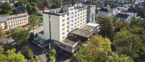 A multi-story building with a flat roof, surrounded by trees and other buildings.